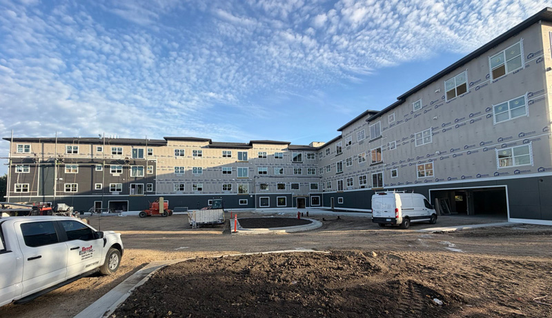 The Oaks II building under construction, featuring a multi-story exterior, installed windows, and an expansive courtyard, with an anticipated opening in May 2027.
